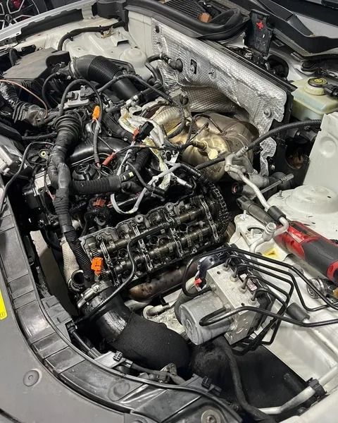 Engine bay of a car with exposed engine components. Black hoses, silver metal, and a red power tool are visible.