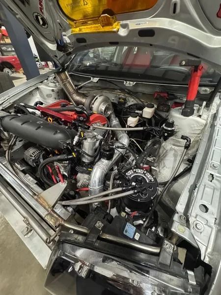 Silver car engine with turbocharger and custom components. Hood open, mechanics work.