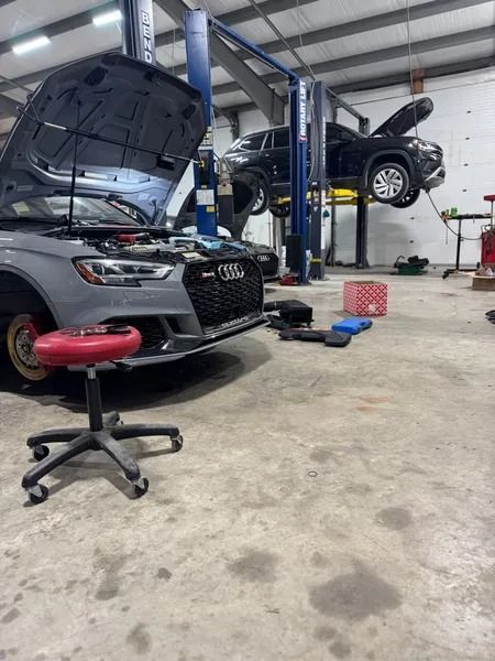 An Audi and a Jeep elevated in a garage. Mechanic's stool, tools, and equipment on the floor.