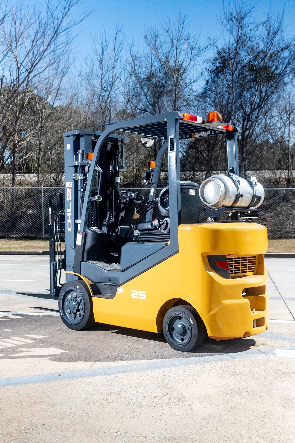 Yellow forklift carrying propane tanks in an outdoor lot with trees in the background