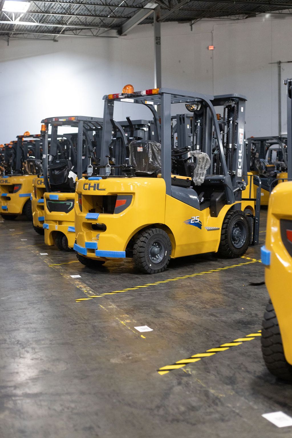 Yellow forklifts parked in a warehouse, lined up on a concrete floor under overhead lights.