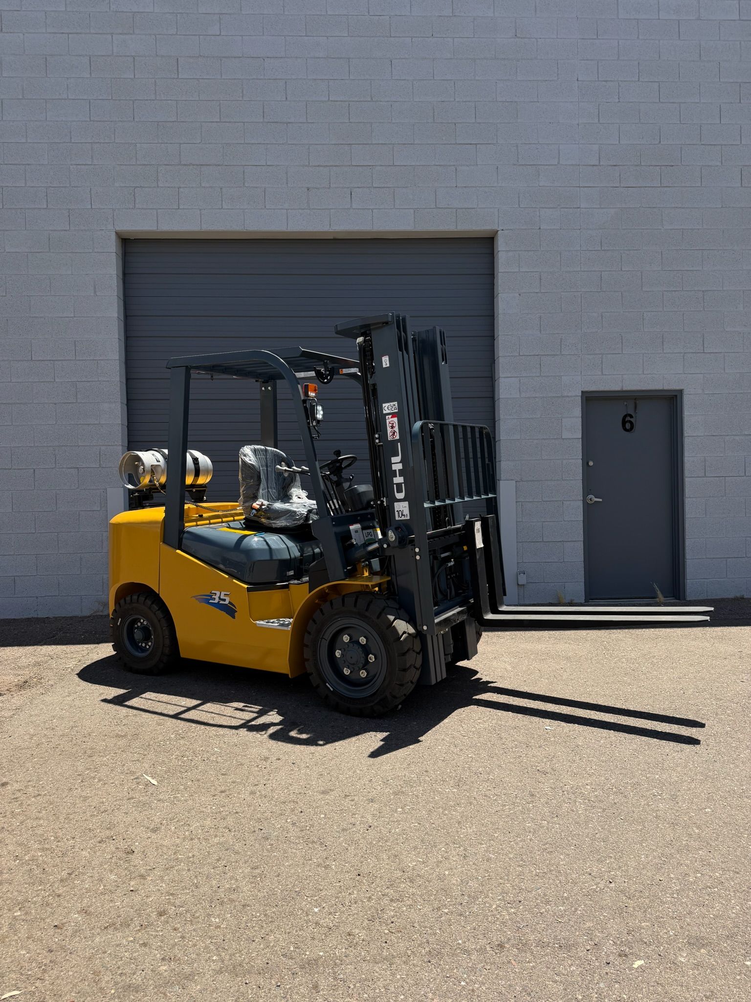 Yellow forklift parked outside a gray warehouse door on a gravel lot.