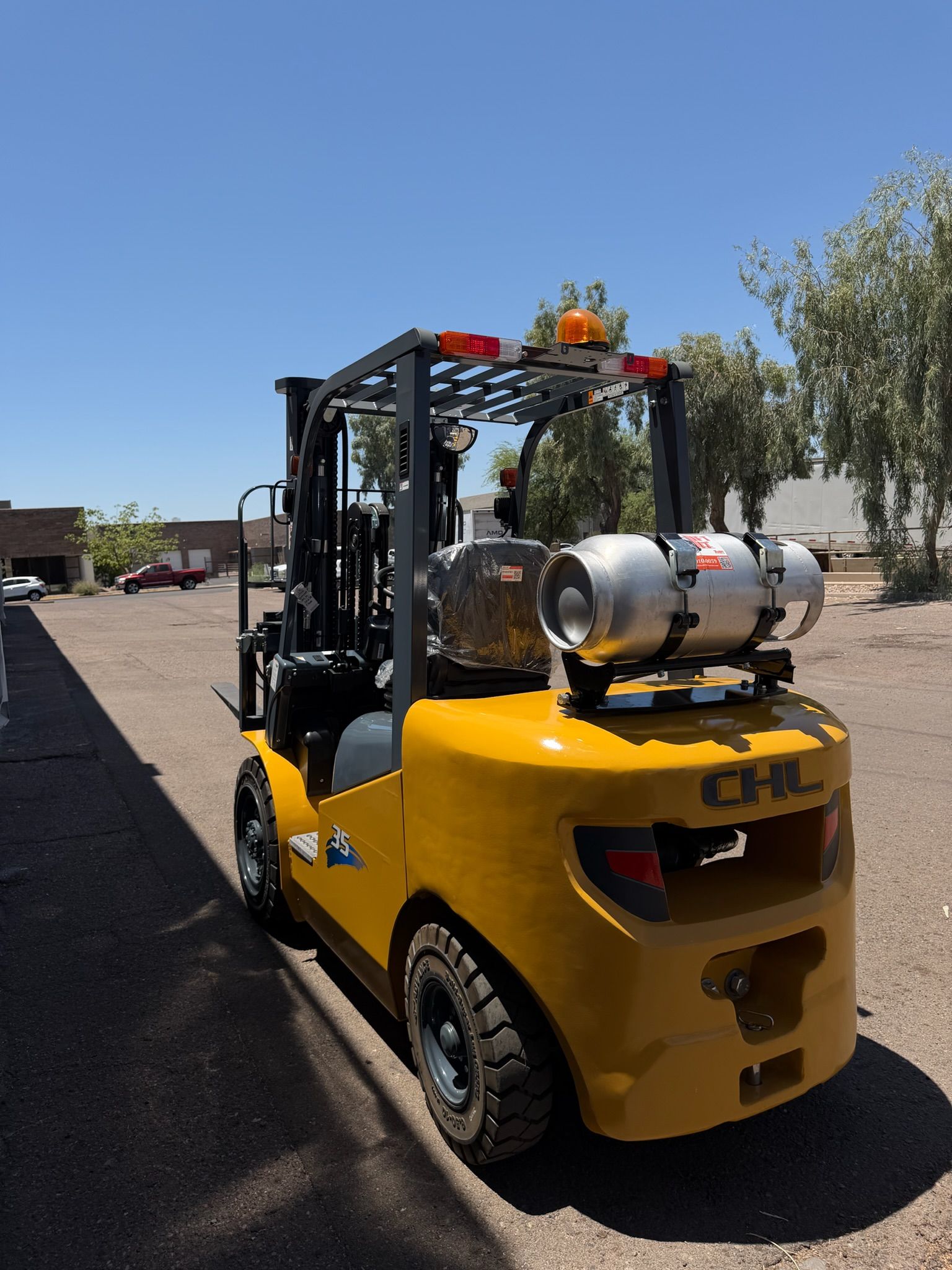 Yellow forklift carrying a propane tank on a sunny outdoor lot