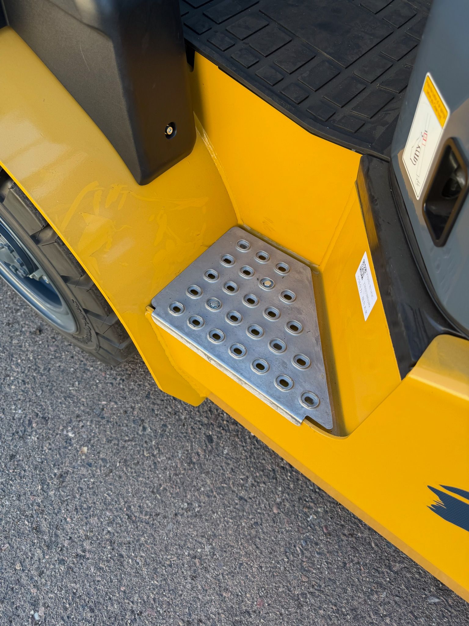 Yellow vehicle step with silver perforated footplate beside a tire on asphalt