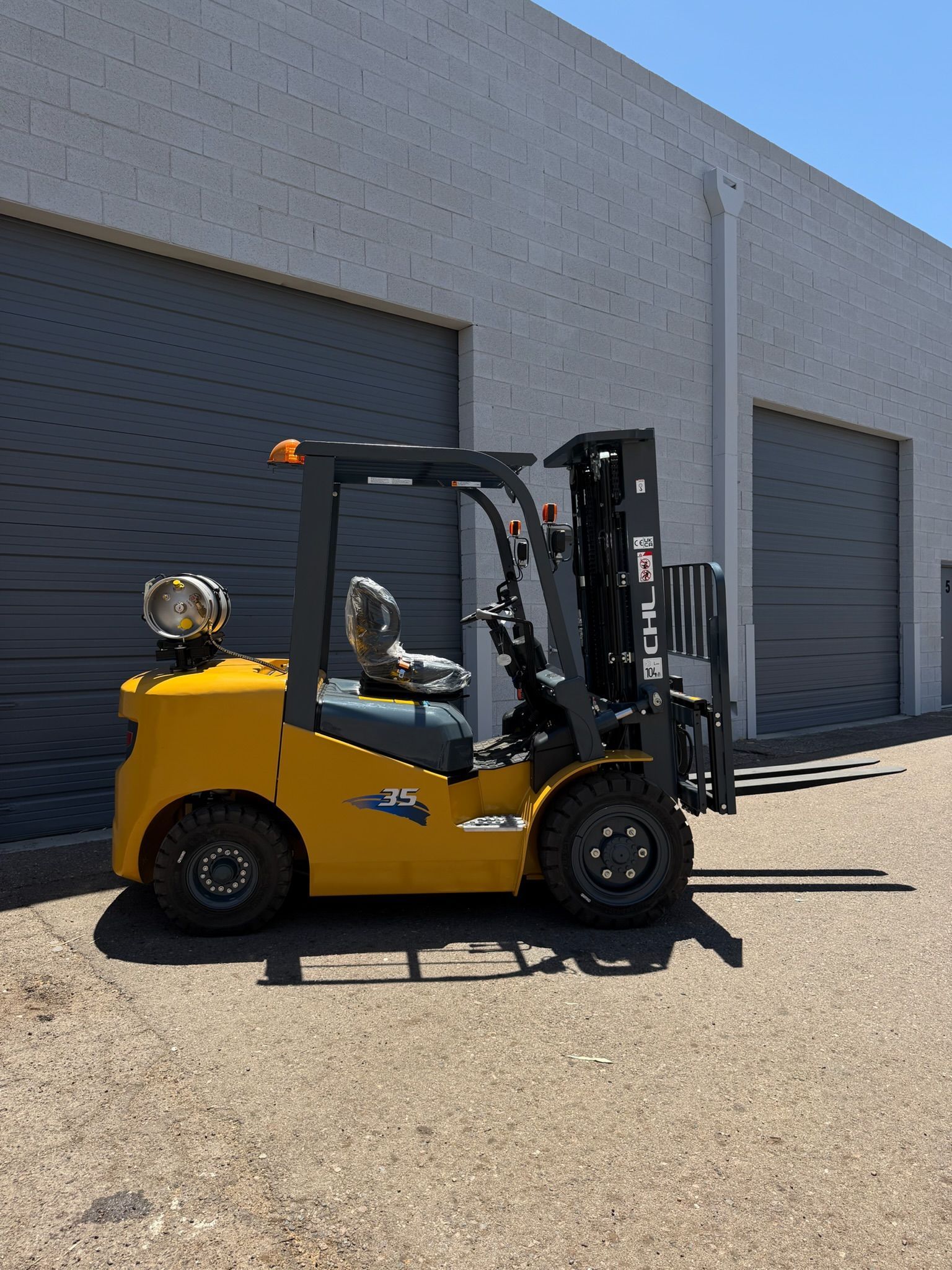 Yellow forklift parked outside a warehouse with closed gray doors in bright sunlight.