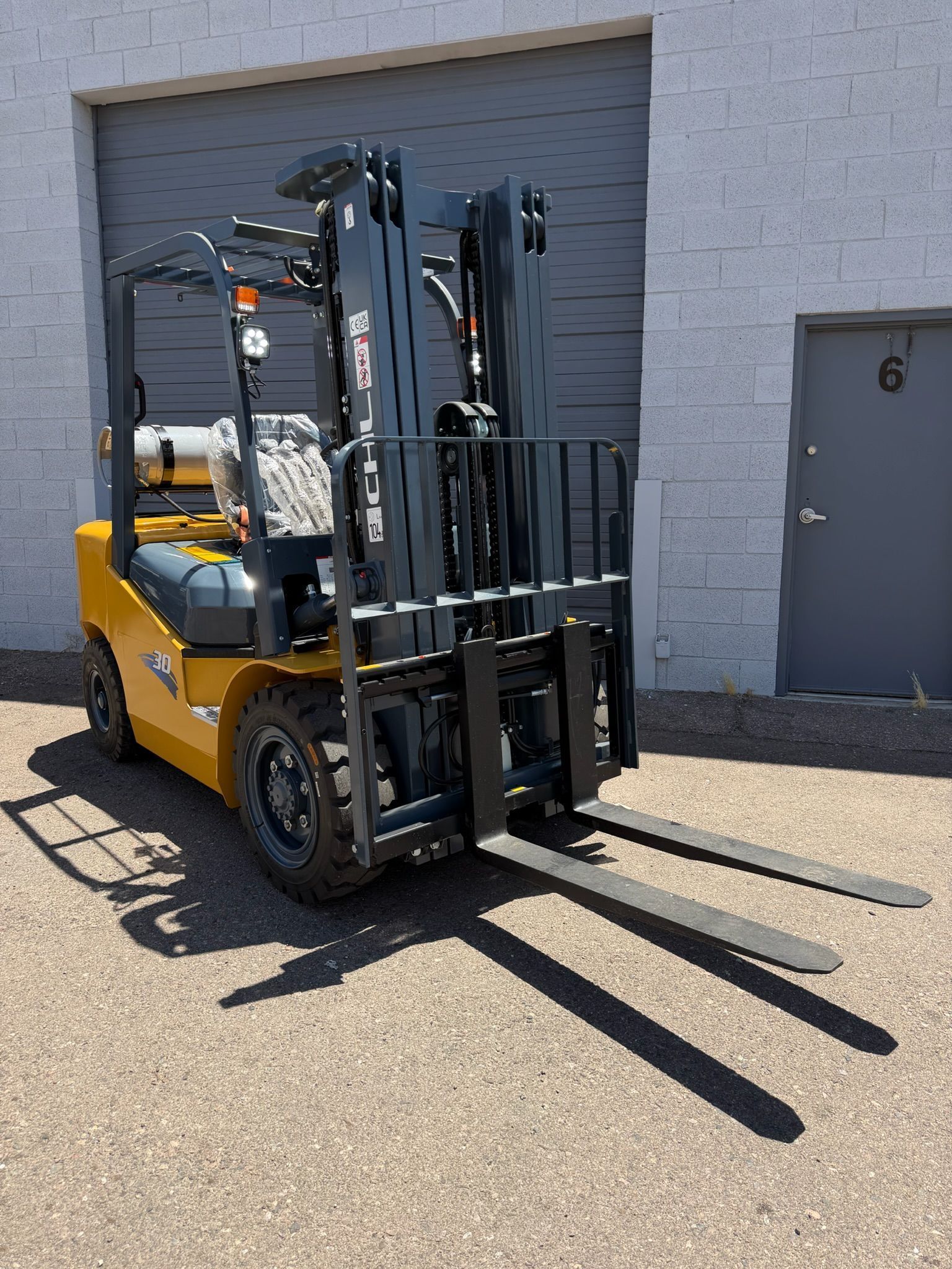 Yellow forklift parked outside a warehouse beside a gray door, with raised forks facing forward