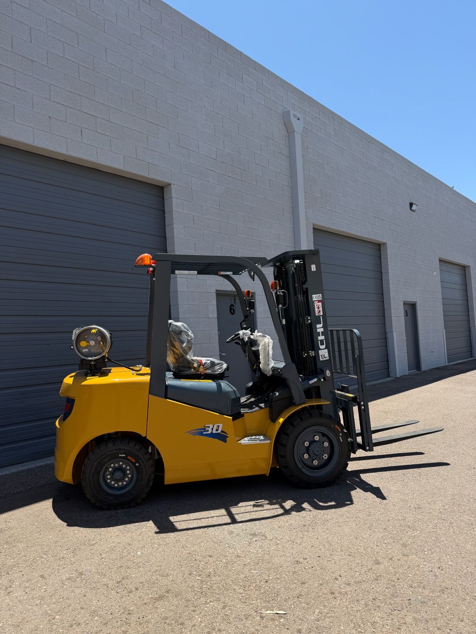 Yellow forklift parked outside gray warehouse loading bays under a clear blue sky.