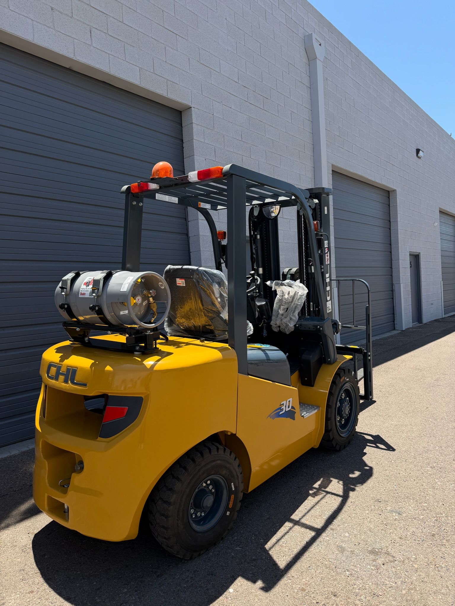 Yellow forklift parked outside a gray warehouse, with orange warning lights on top.