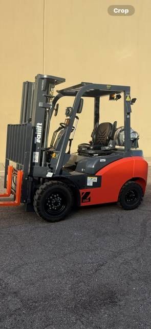 Red and black forklift parked beside a beige wall on asphalt.