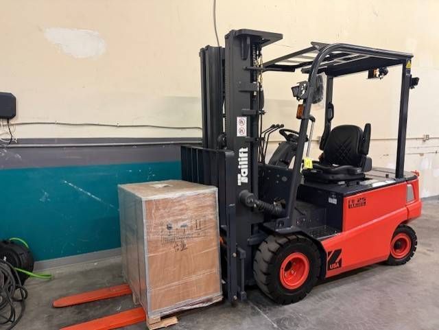 Red forklift lifting a wooden crate on red forks in a warehouse aisle.