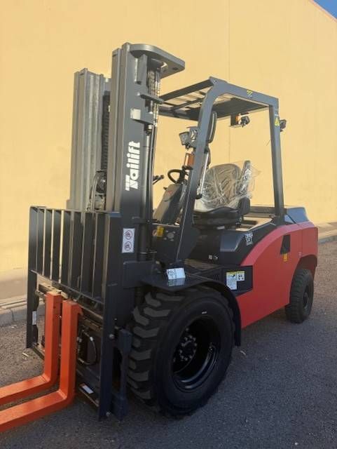 Red forklift with raised forks parked on pavement against a yellow wall