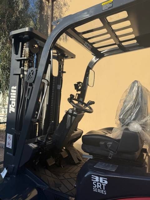 Black forklift with plastic-covered seat and steering wheel against a yellow wall.