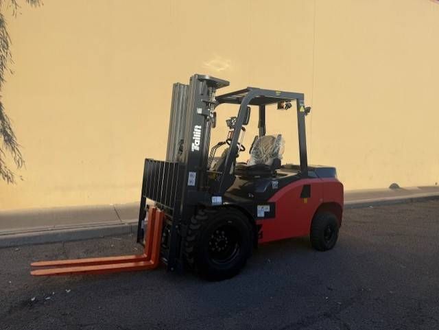 Red forklift parked on pavement against a yellow wall at sunset