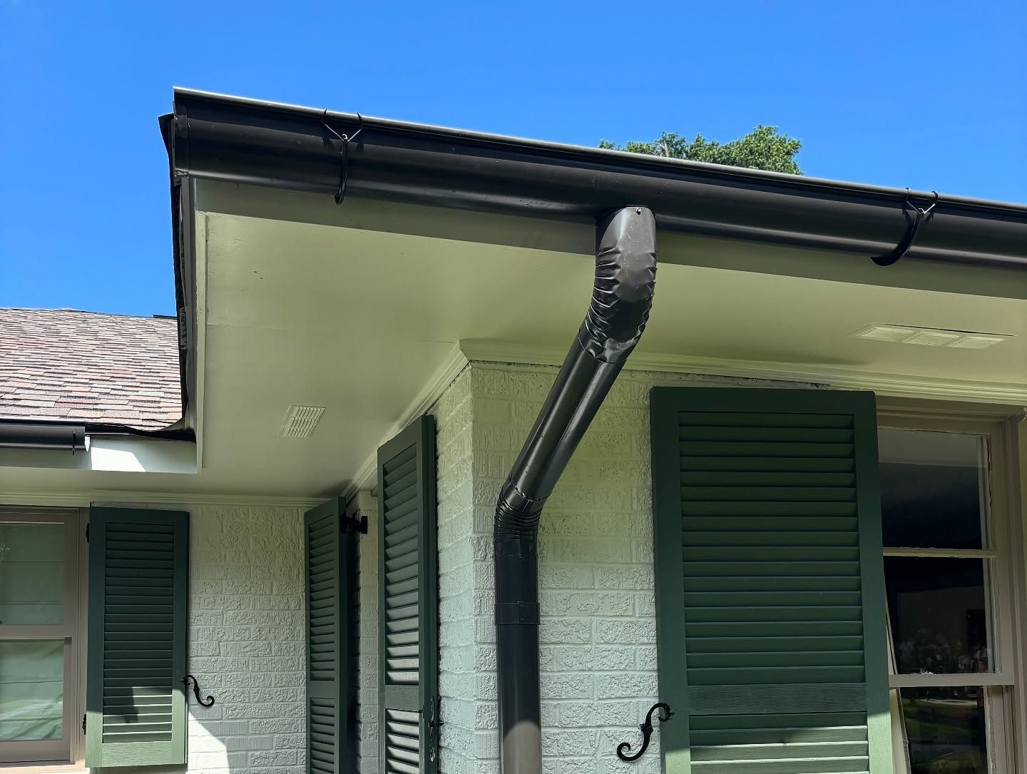 Black gutters on a light-colored building, dark green shutters, blue sky.
