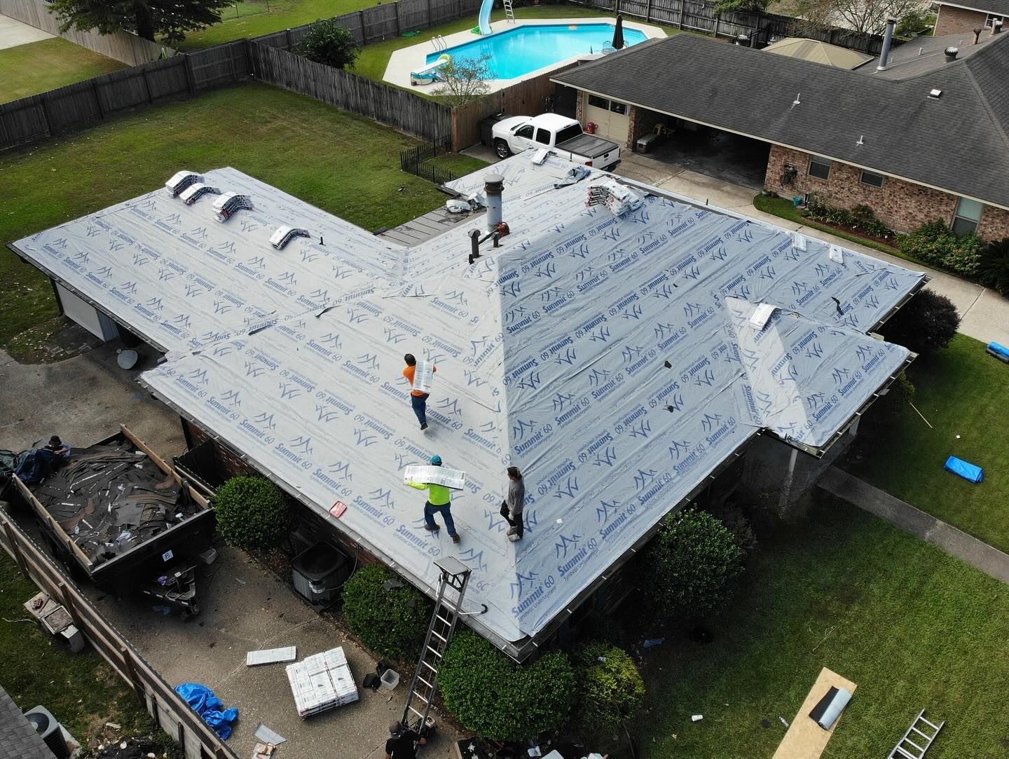 Roofers installing a new roof on a house with a pool in the backyard; sunny day.