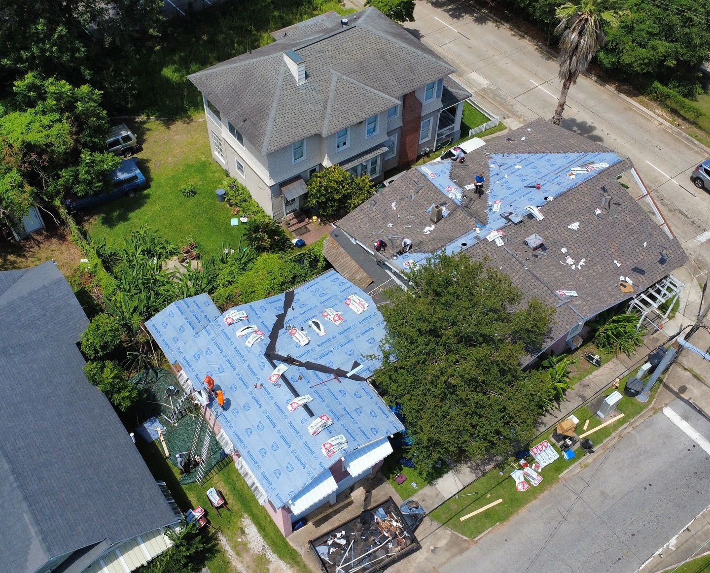 Aerial view of storm-damaged homes with missing roofs, debris scattered, and some areas covered in blue tarp.