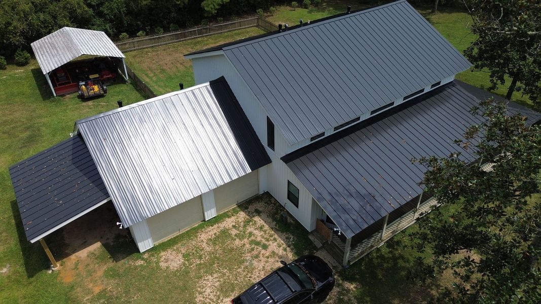 Aerial view of a white house with a metal roof, black car in driveway, and a shed in a grassy yard.