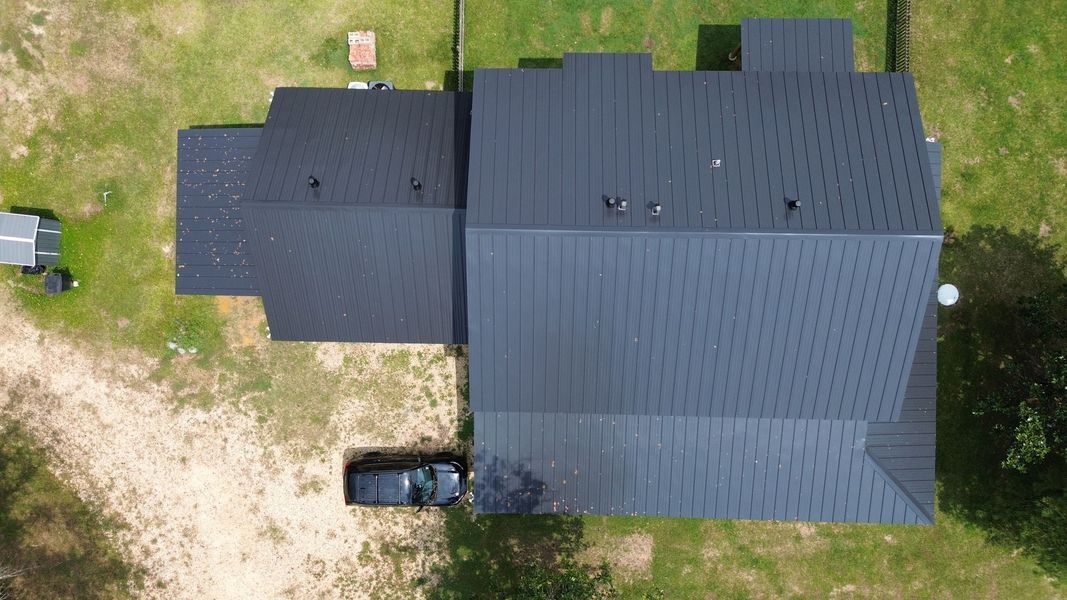 Overhead view of a dark-roofed house with a car parked in the driveway, surrounded by green grass.