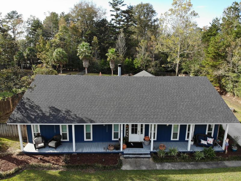 Blue house with white porch, dark gray roof, and fall foliage.