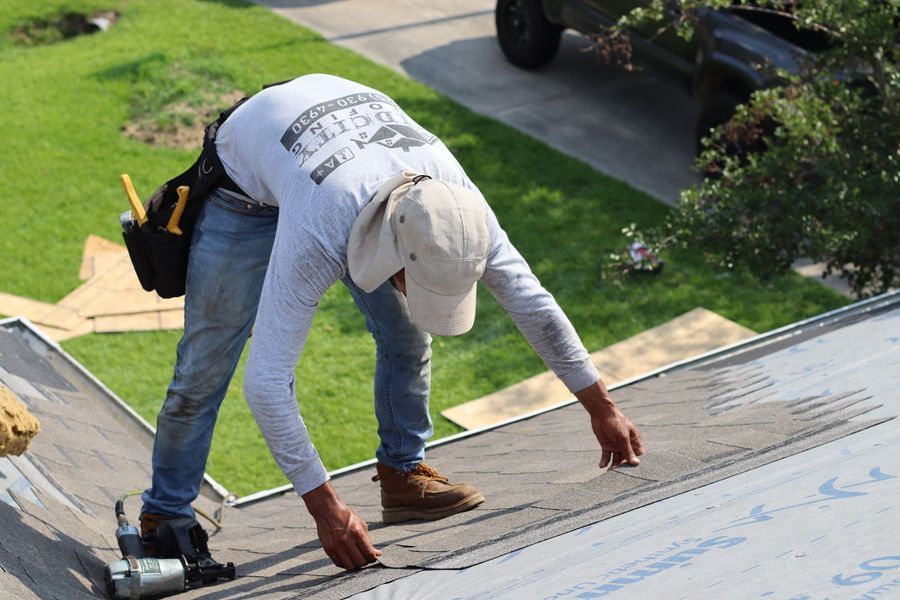 Roofer on a roof, installing materials, wearing hat, safety gear.