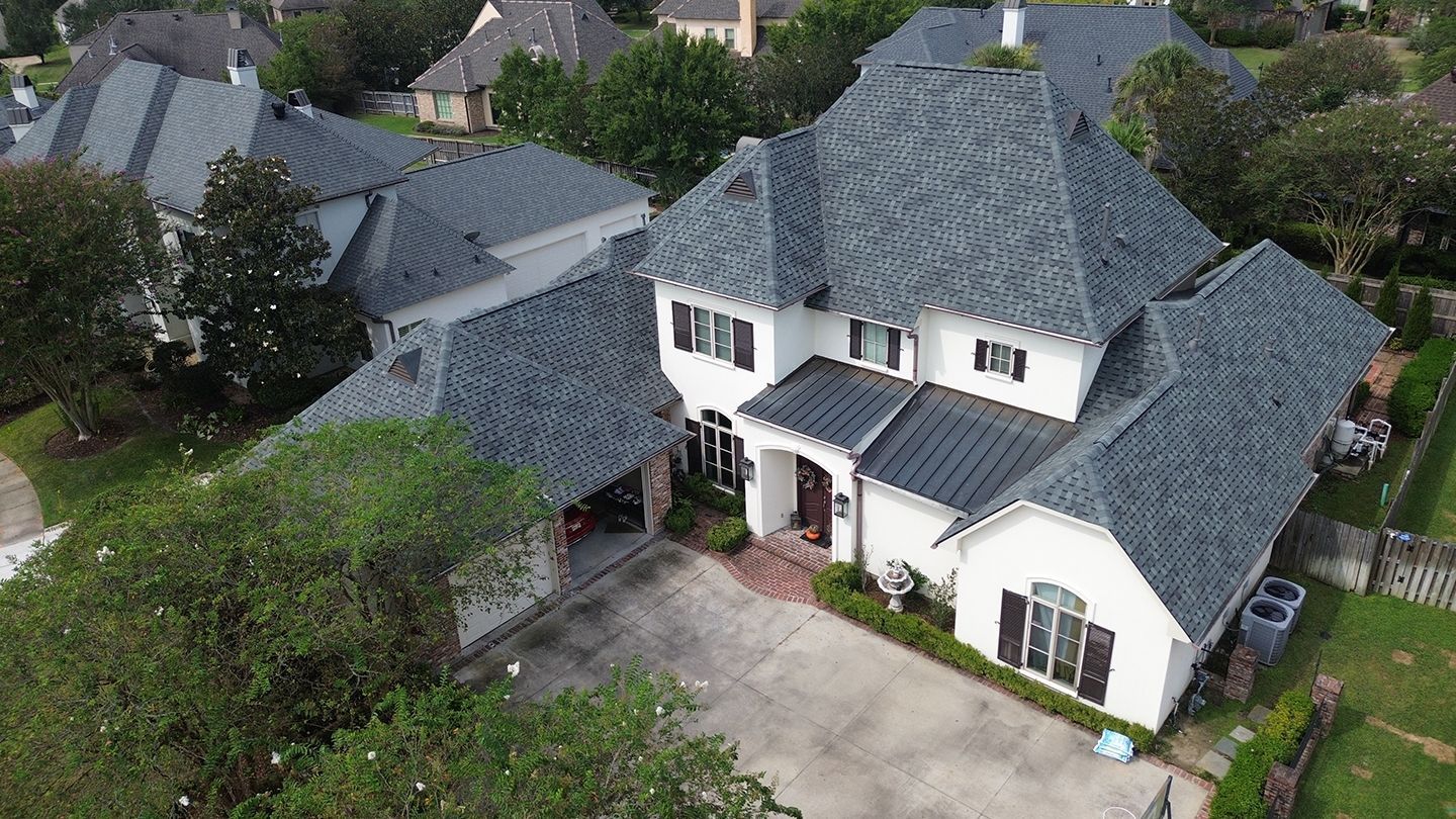 Aerial view of a white two-story house with a gray roof and a driveway, surrounded by trees.