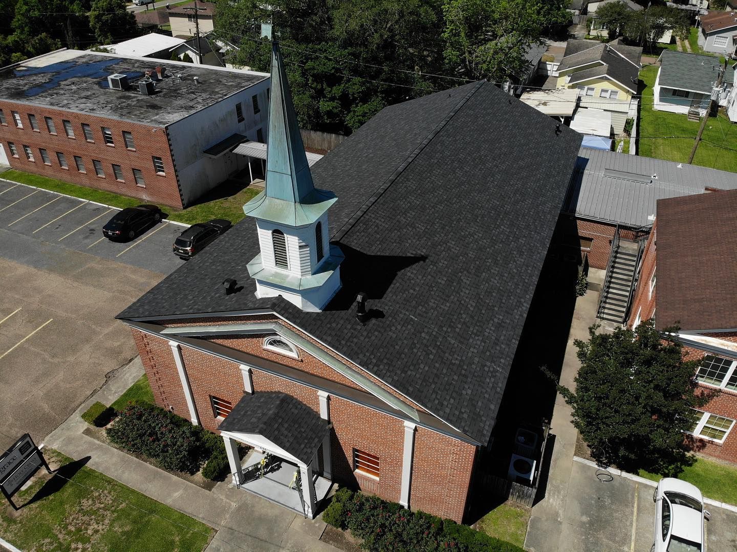 Aerial view of a red brick church with a white steeple and dark gray roof.