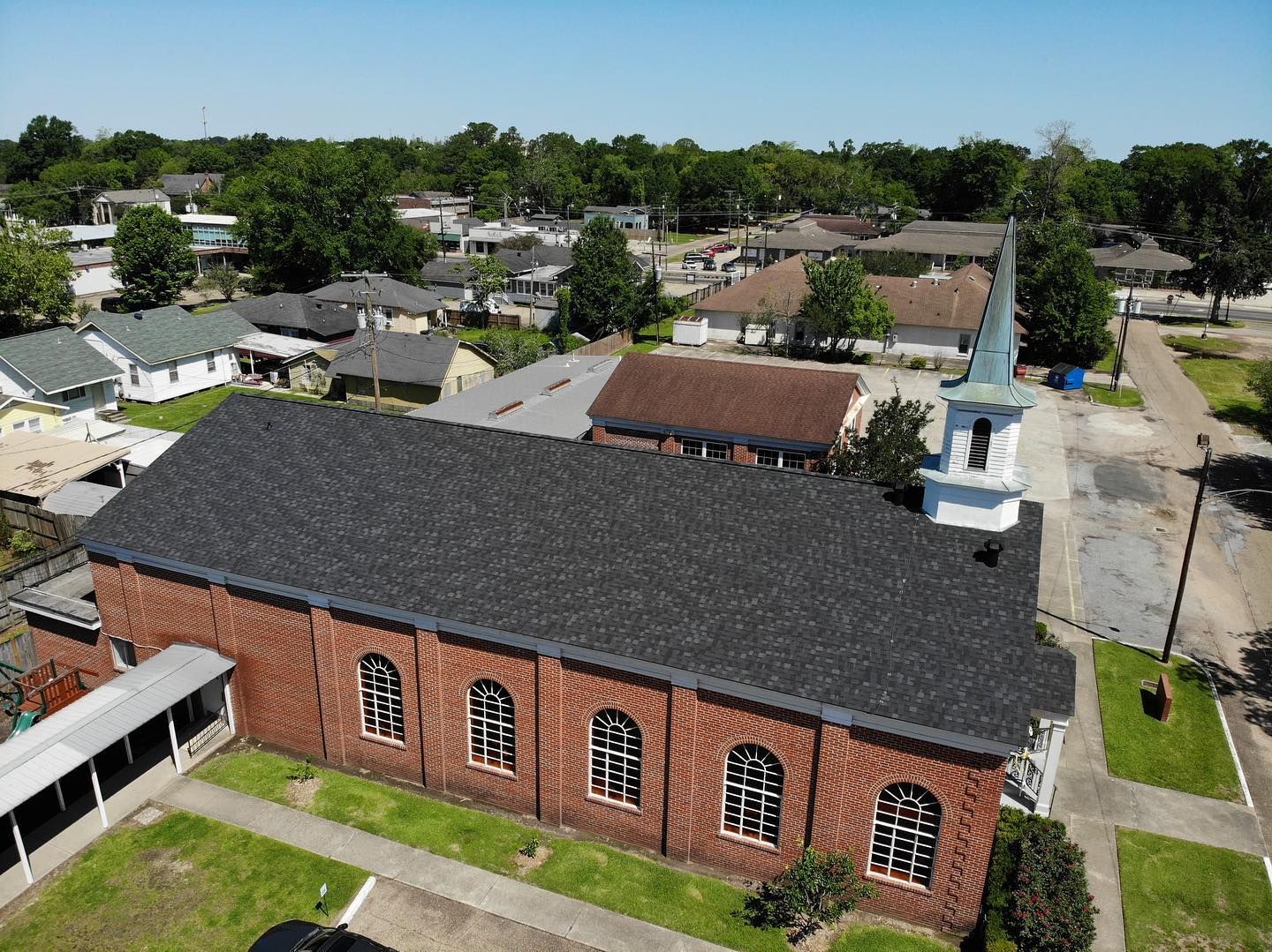 Aerial view of a red brick church with a black roof and a white steeple in a residential area.