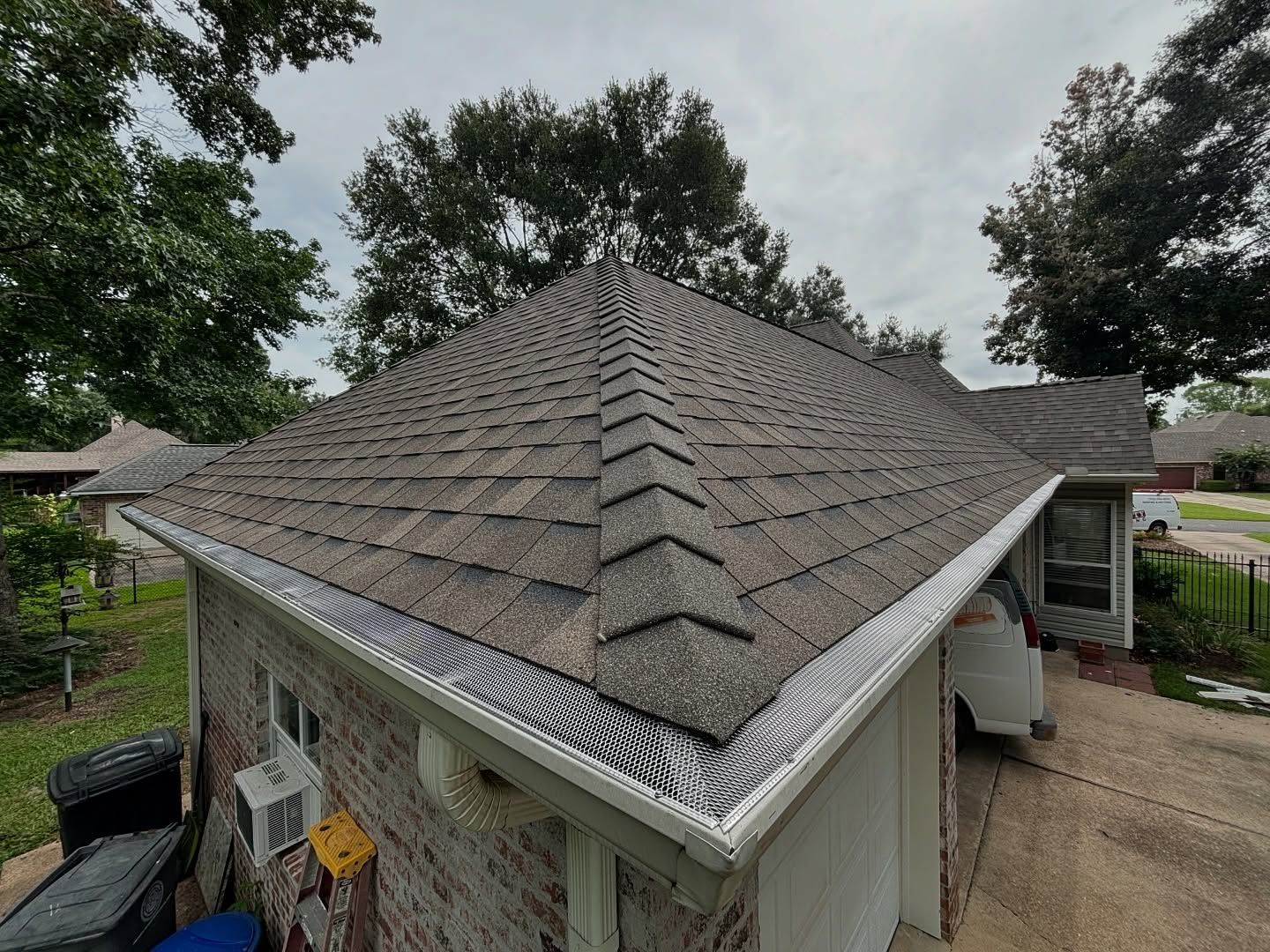 A brick house with a newly shingled roof and gutters, under a cloudy sky.