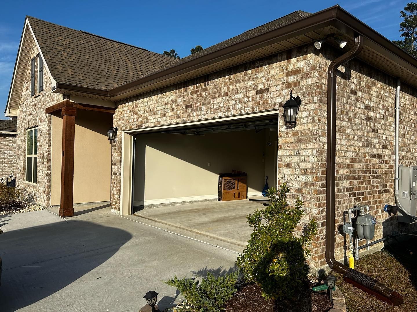 A brick house with an open garage door on a sunny day. Brown gutters and trim.