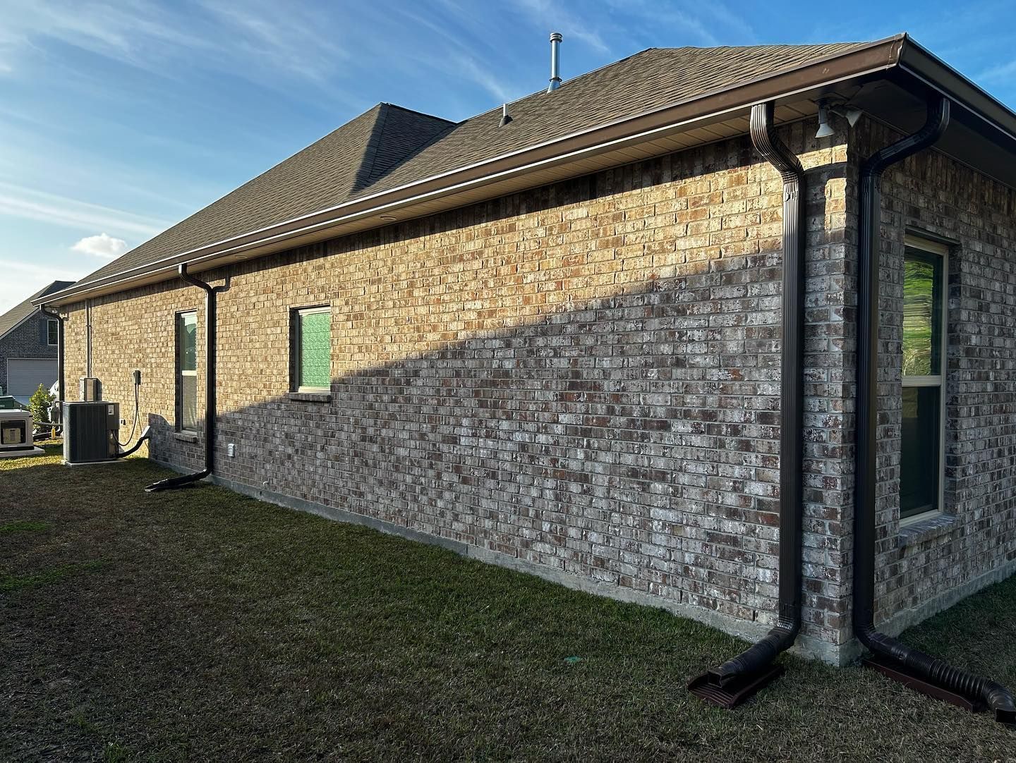 Brick house exterior with brown gutters and roof, green lawn under a blue sky.
