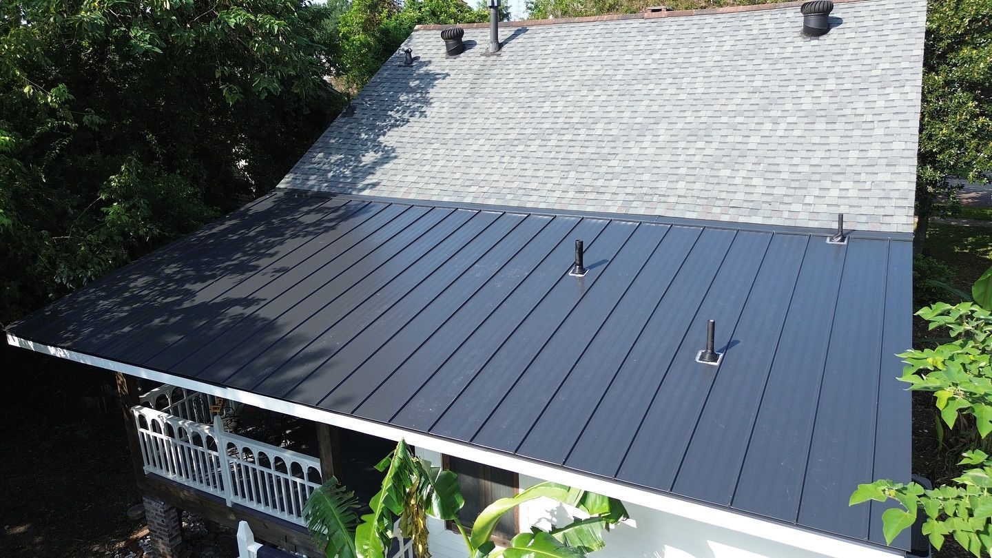 Black metal roof on a white house, trees surround.