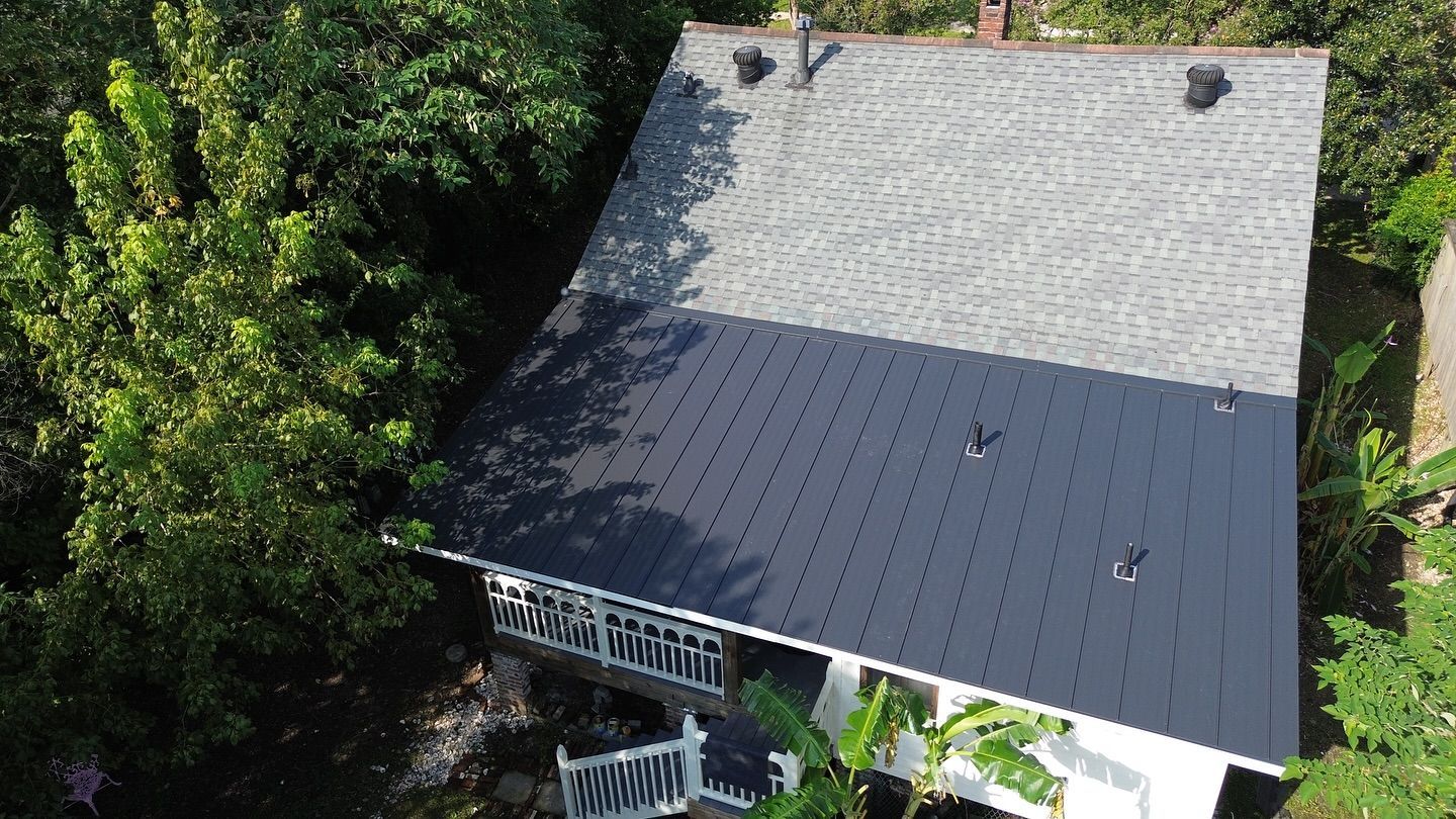 Overhead view of a house with a dark gray roof, some surrounded by green trees.