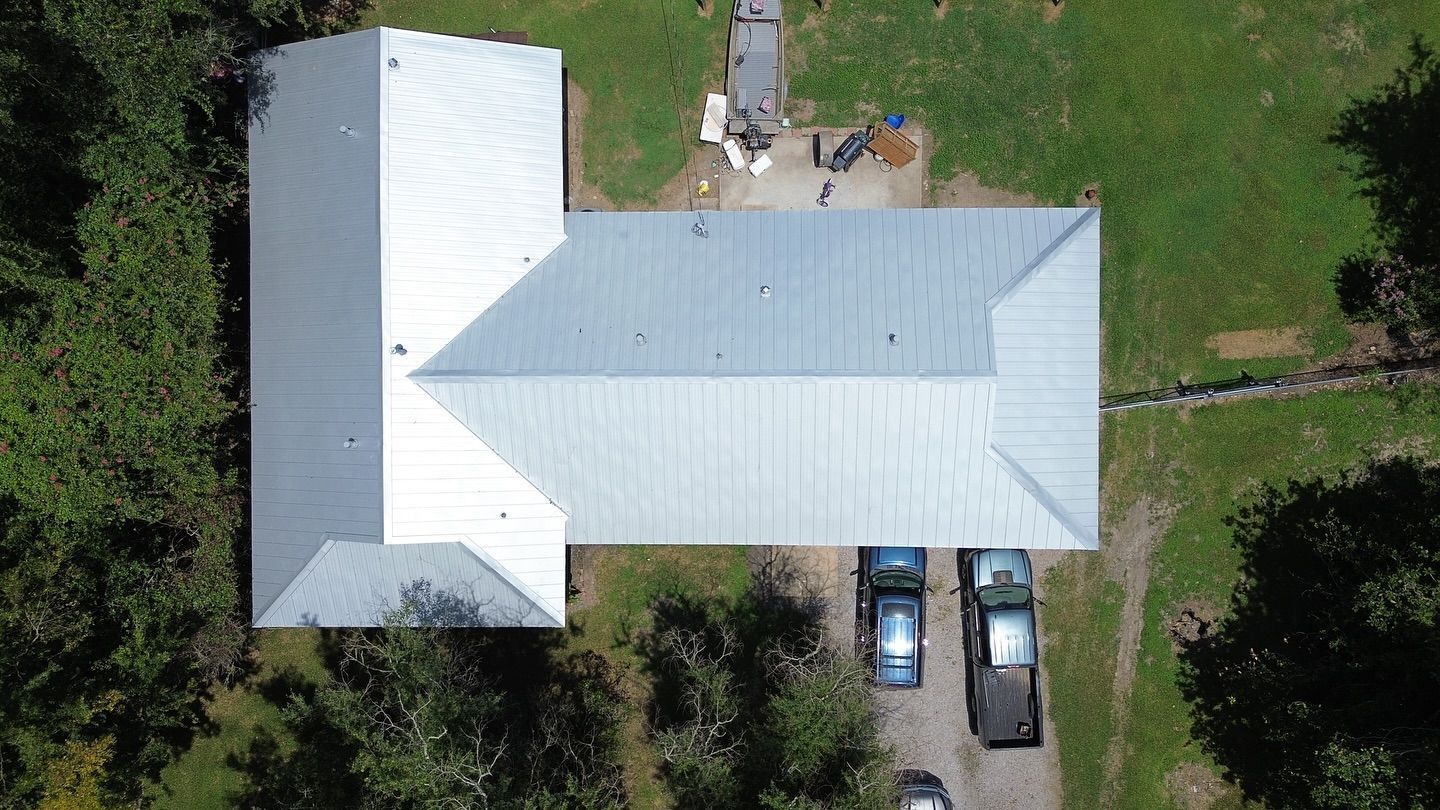 Aerial view of a building with a silver metal roof and several parked vehicles on a gravel driveway.