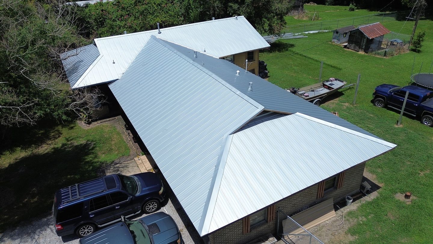 Aerial view of a house with a shiny, silver metal roof. Parked cars in the front on a grassy lawn.