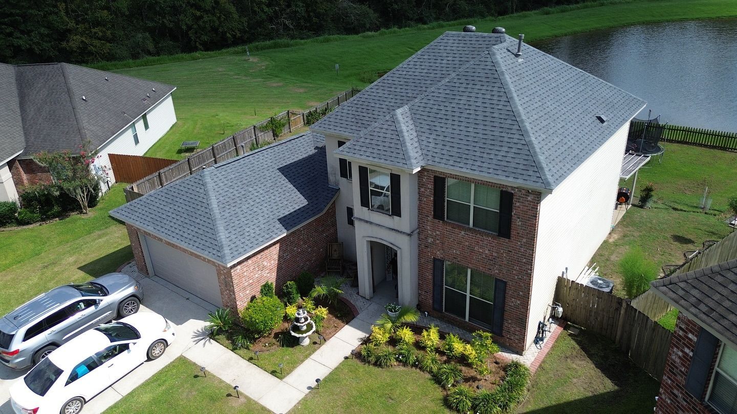 Two-story house with red brick and gray roof, a garage, and two cars parked on the lawn.