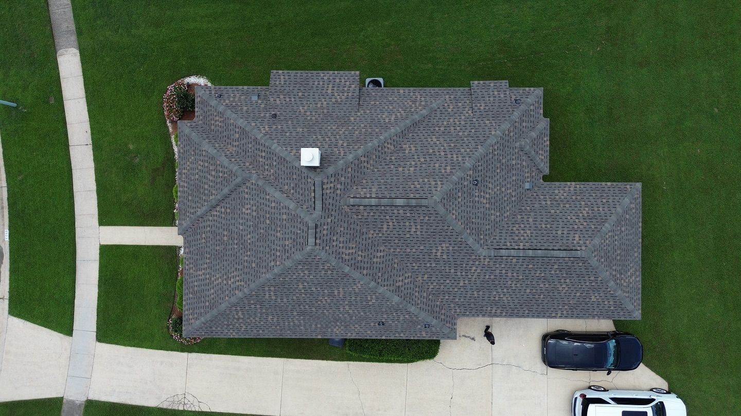 Overhead view of a house with a dark gray roof, surrounded by green grass and a driveway with two cars parked.