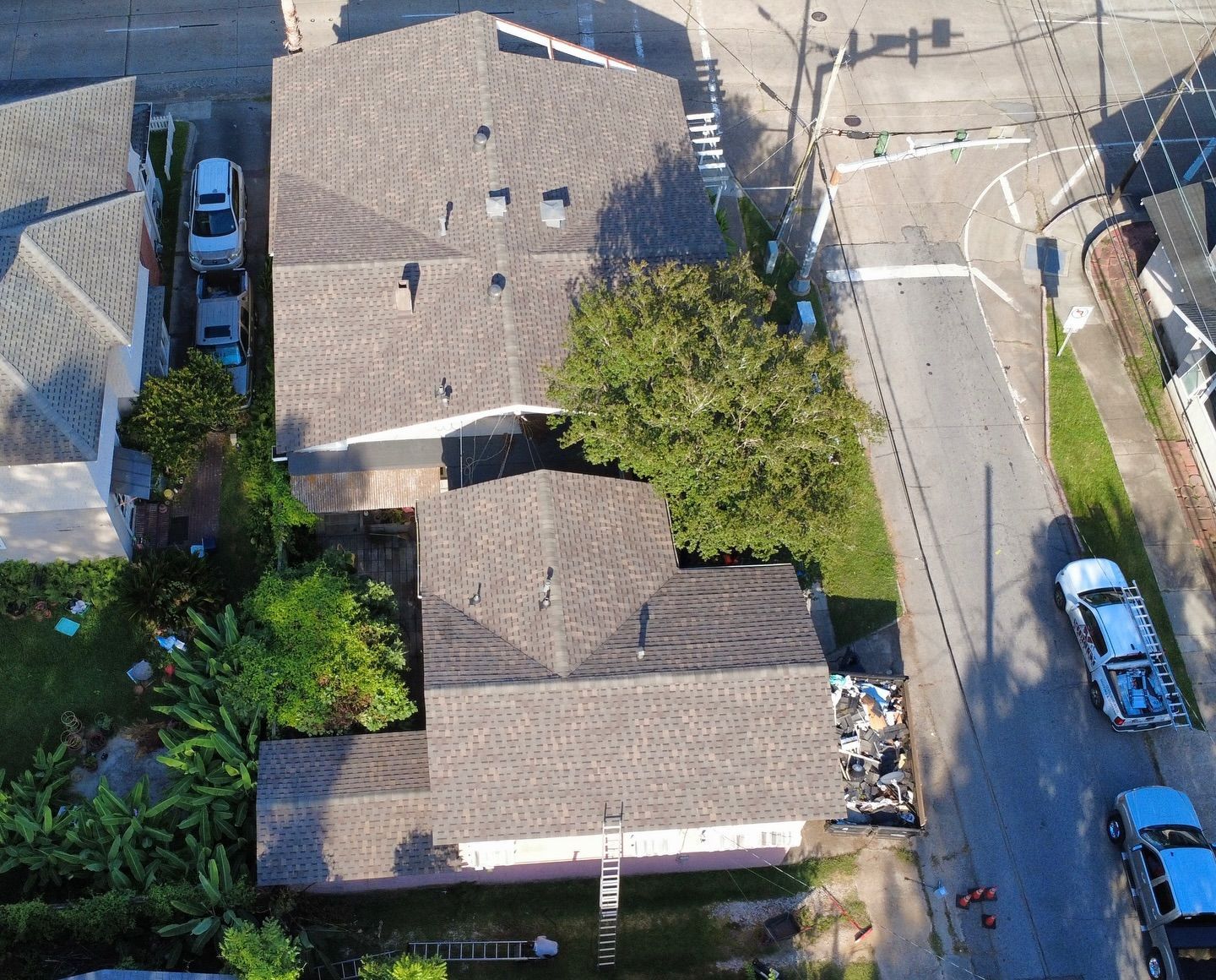 Overhead view of two houses with gray roofs, a tree, and a street with parked cars.
