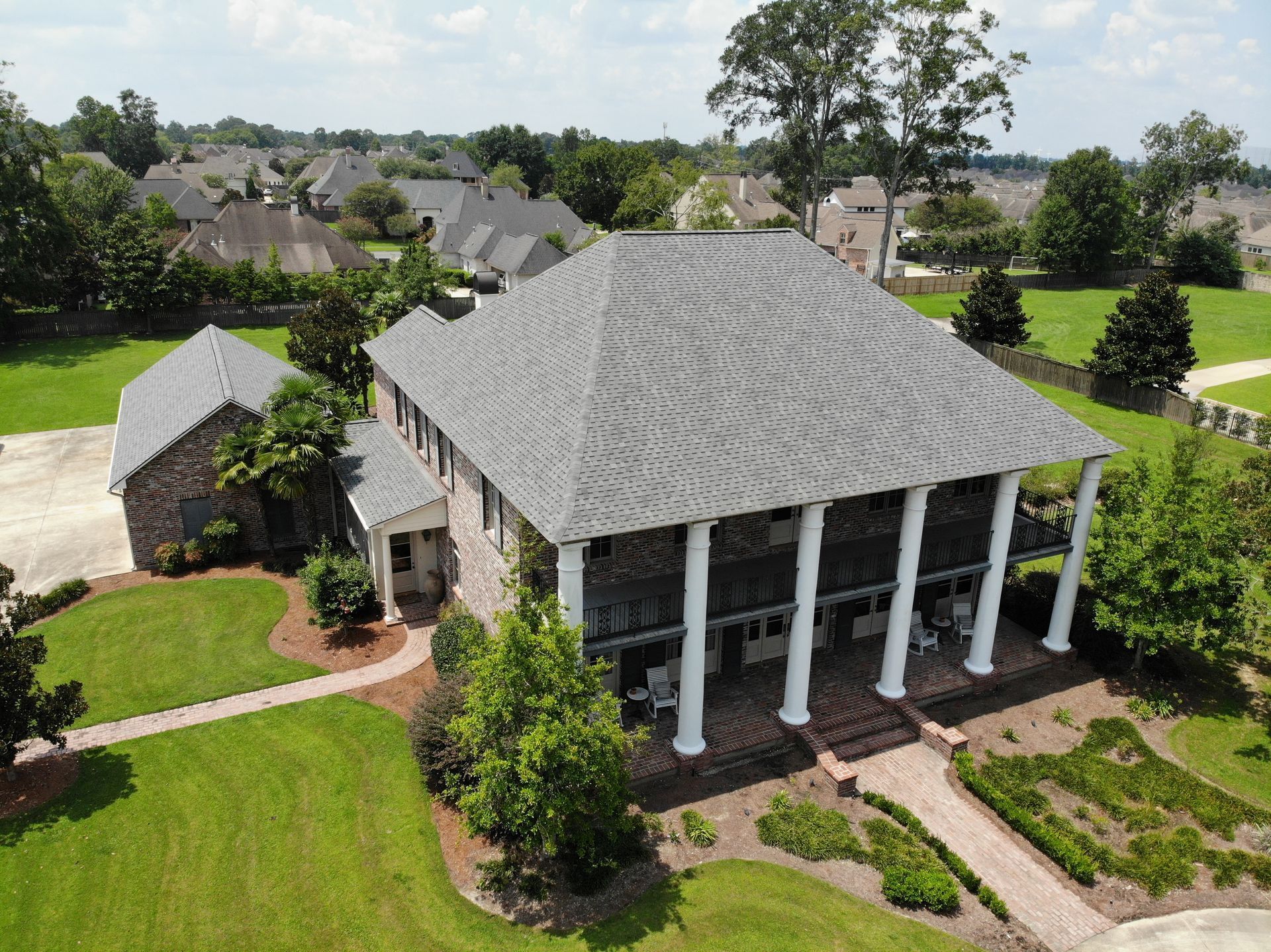 Large house with white columns, brick steps, and a well-manicured lawn in a suburban setting.