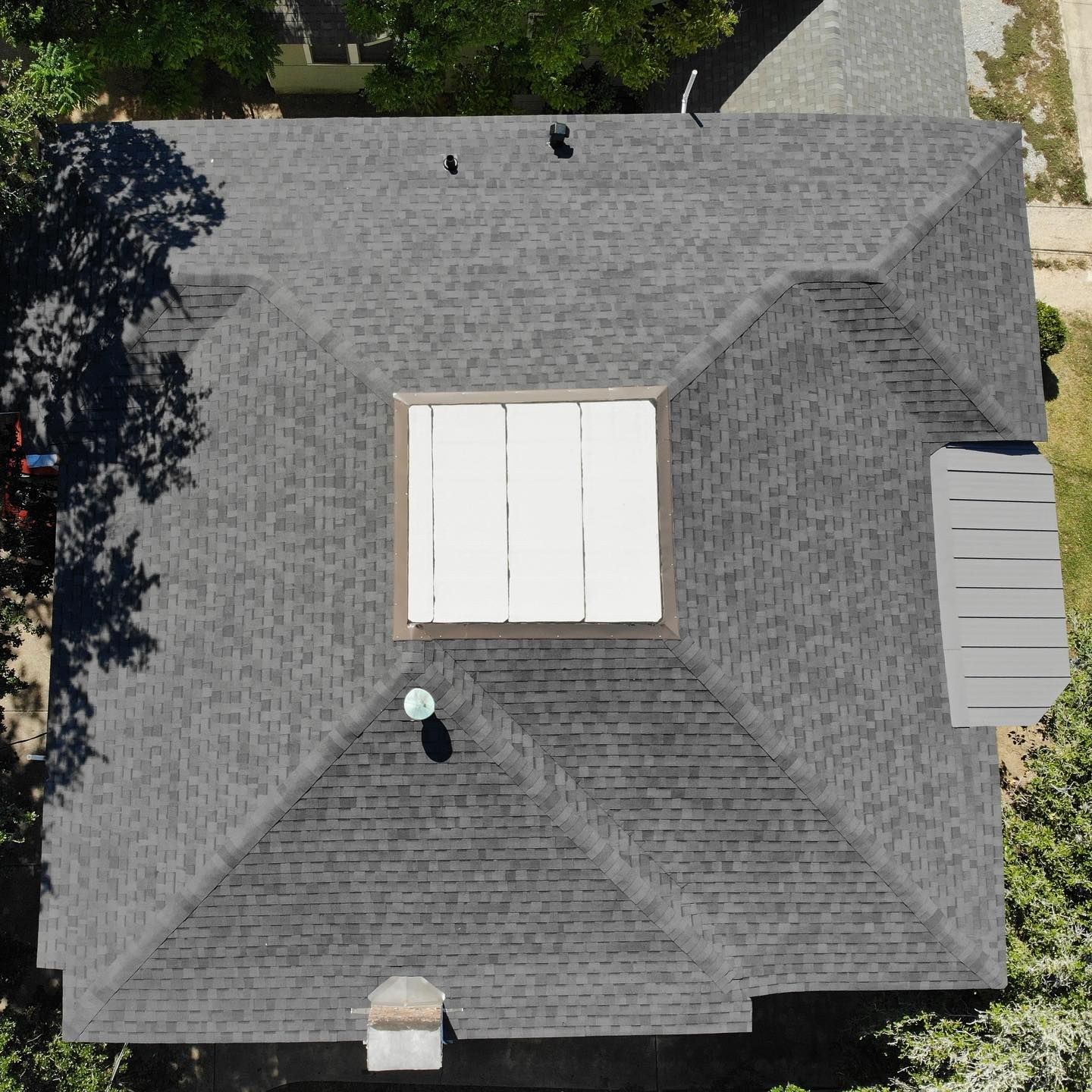 Overhead view of a house with a gray shingled roof, skylight, and trees.