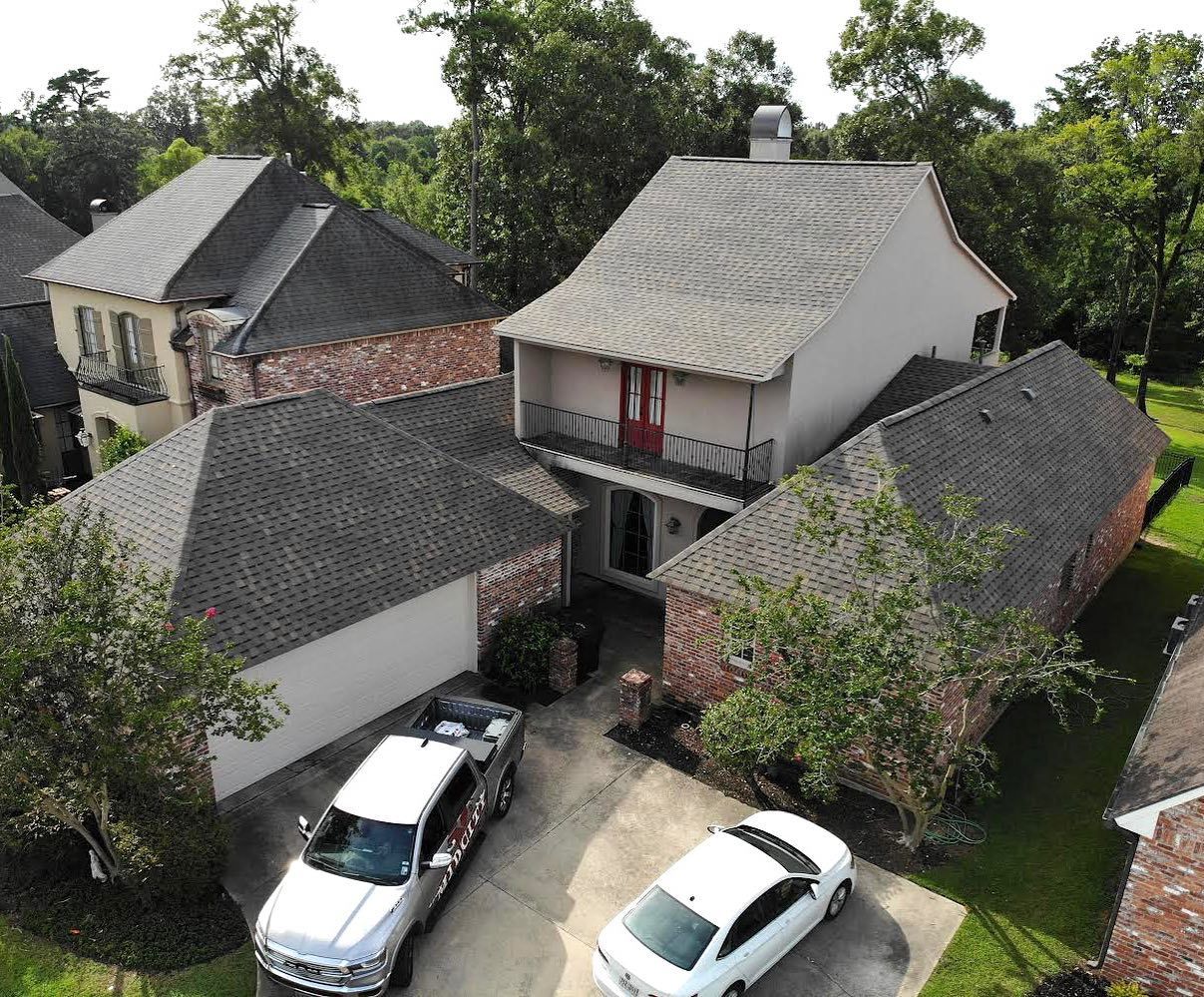 Two-story house with a white car and truck in the driveway. Green yard, brick and grey roof.