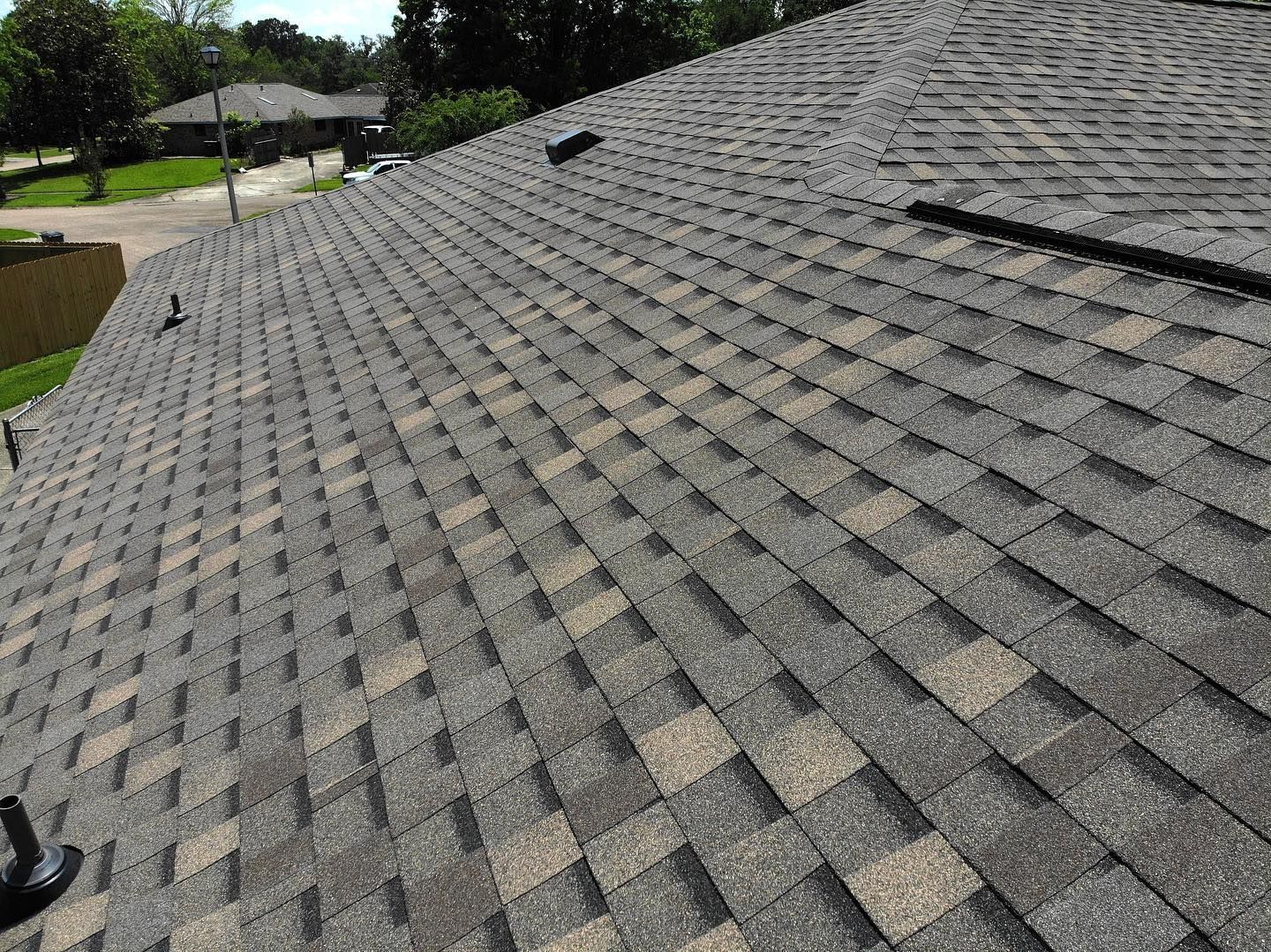 Close-up view of a roof covered with gray and tan asphalt shingles, outdoors in daylight.