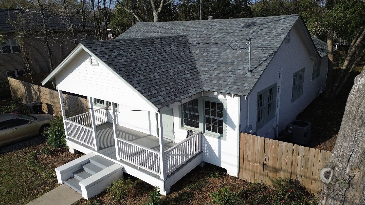 White cottage with porch, gray roof, and wooden fence in a yard.