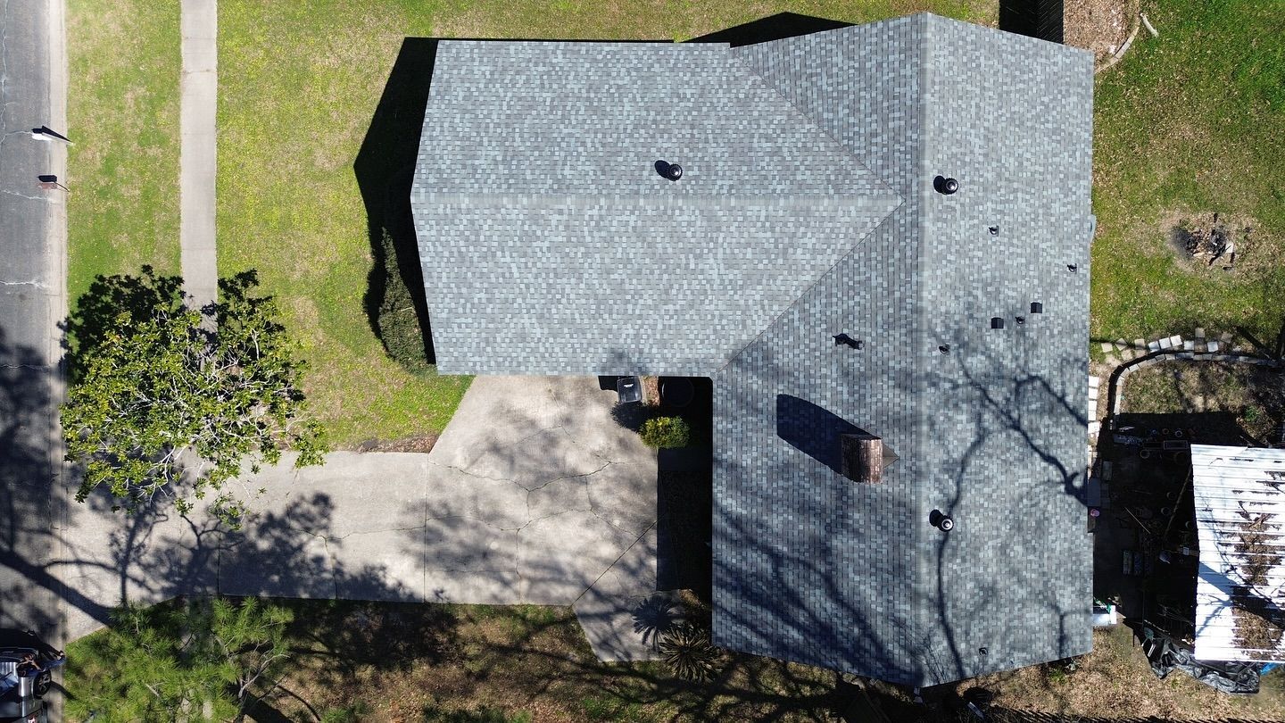 Overhead view of a house with gray roof, brick chimney, and surrounding green lawn and driveway.