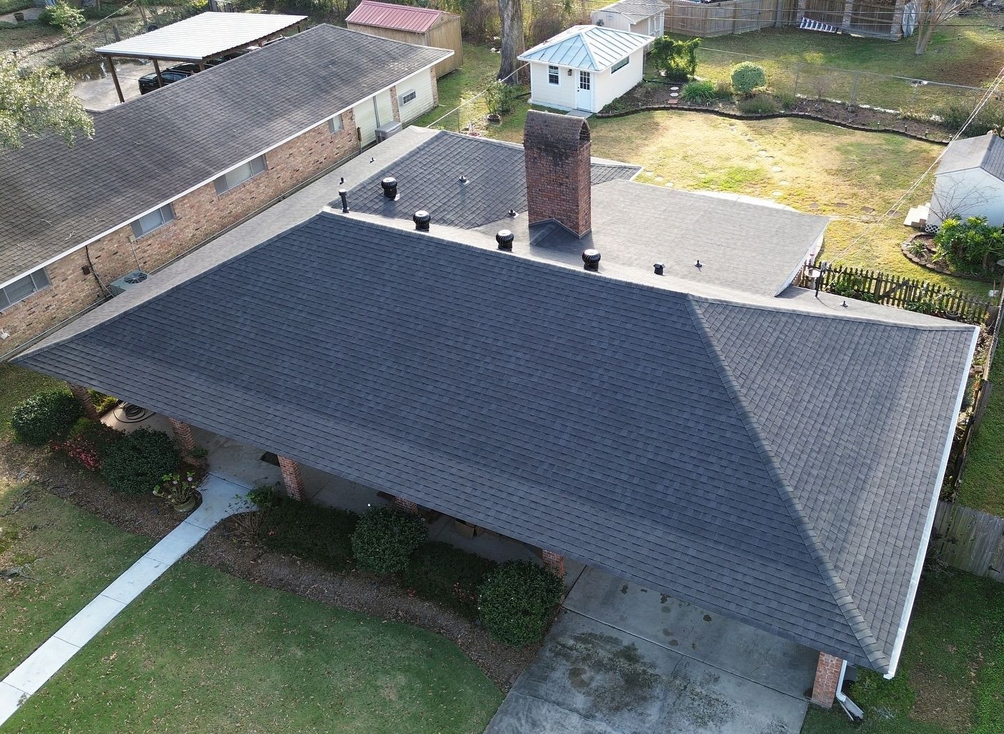 An aerial view of a house with a black shingled roof, brick chimney, and green lawn.