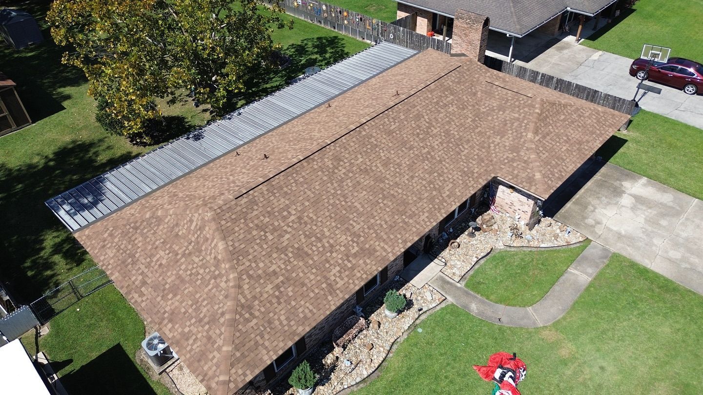 Overhead view of a brown roof with a silver section, surrounded by green grass and a house.