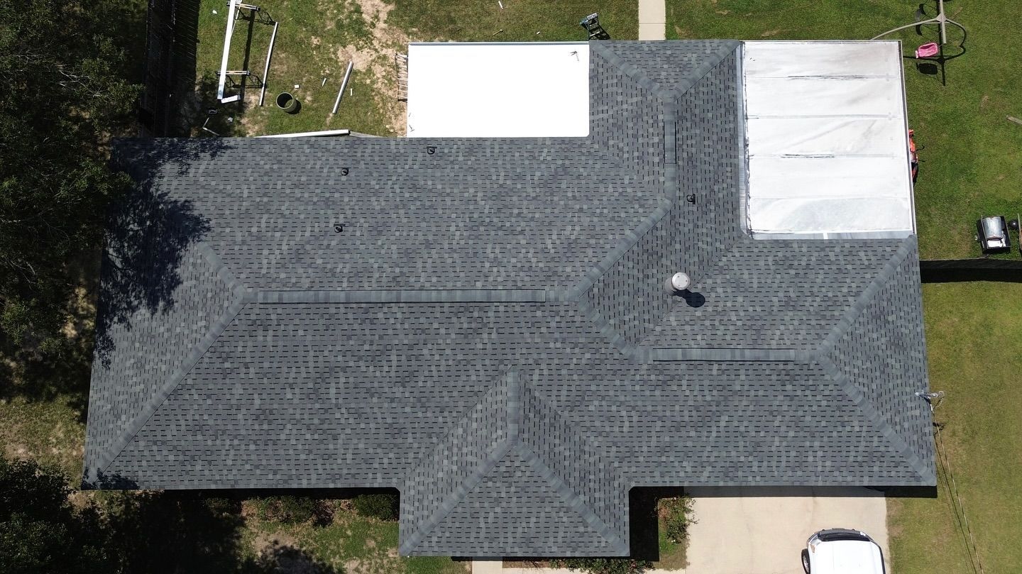 Overhead view of a dark gray shingle roof with white patches; a car is parked in the driveway.