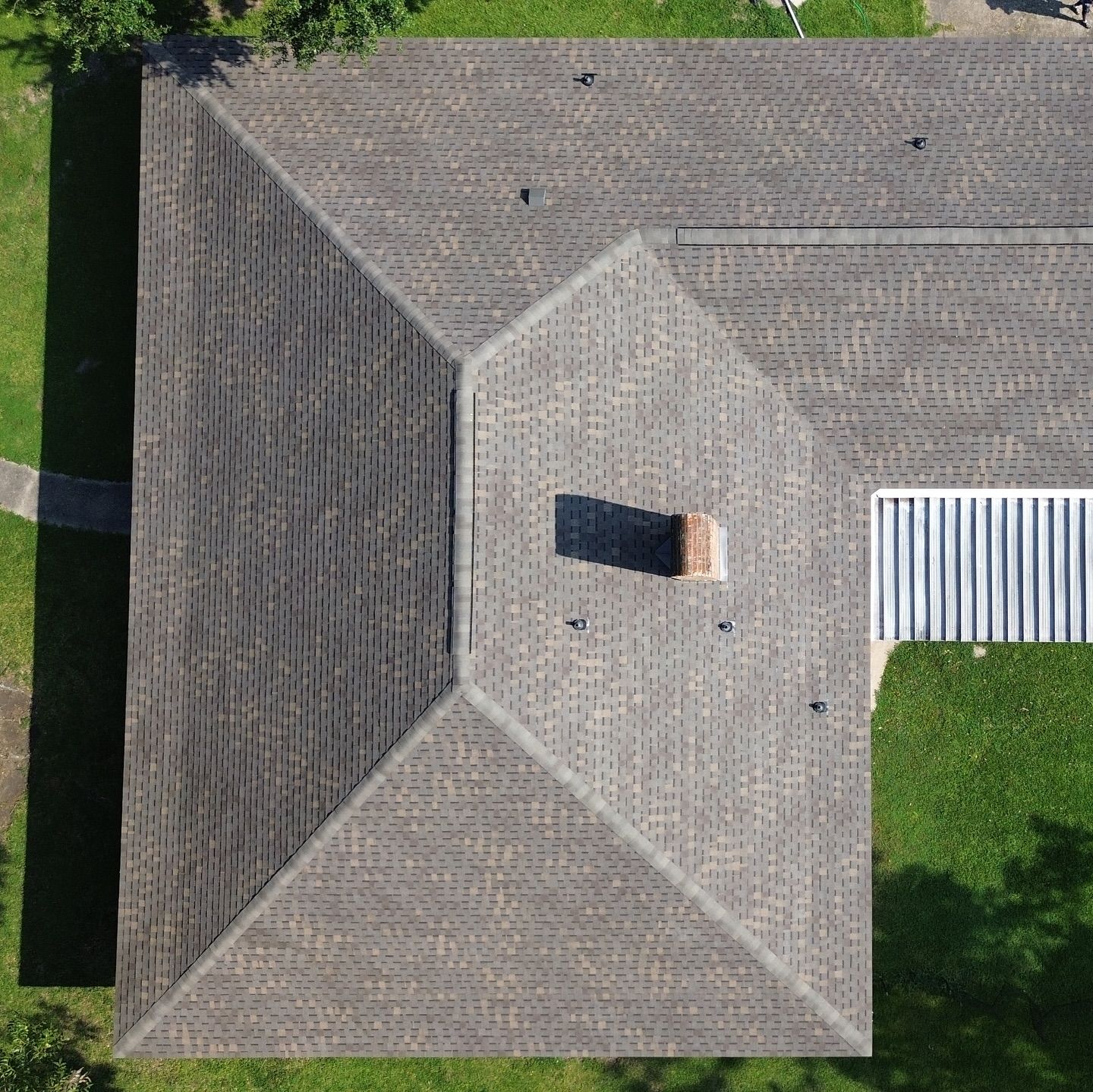 Overhead view of a house with a gray shingled roof, chimney, and white siding on a green lawn.