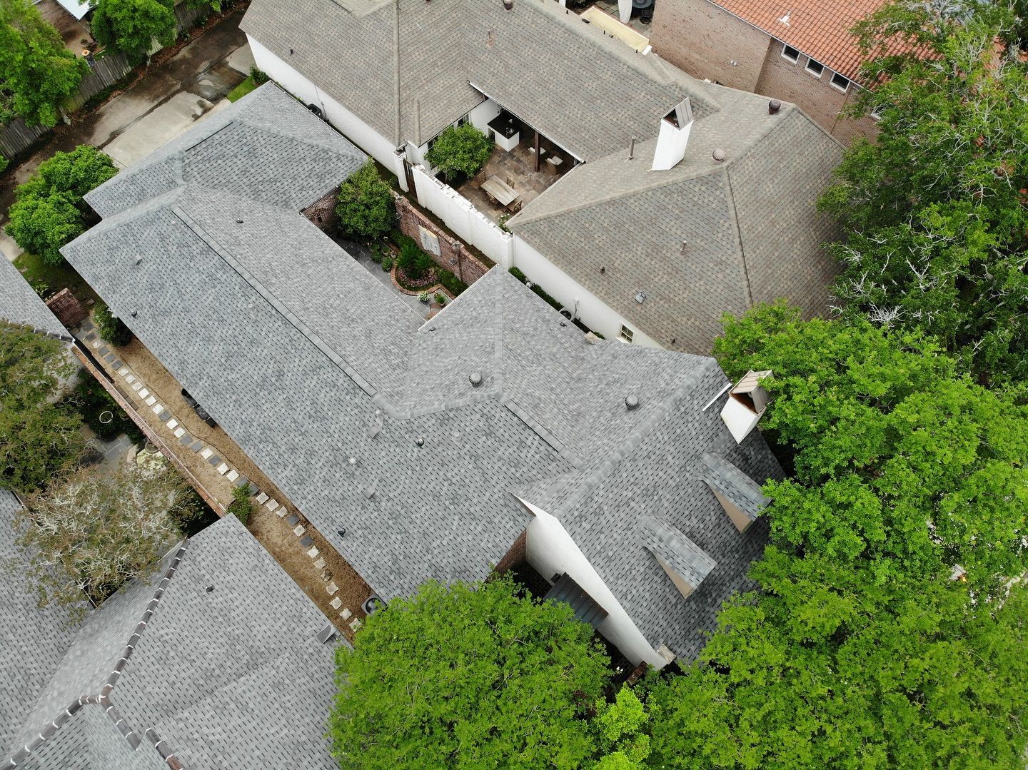 Aerial view of a multi-sectioned house with gray shingle roof, surrounded by trees.