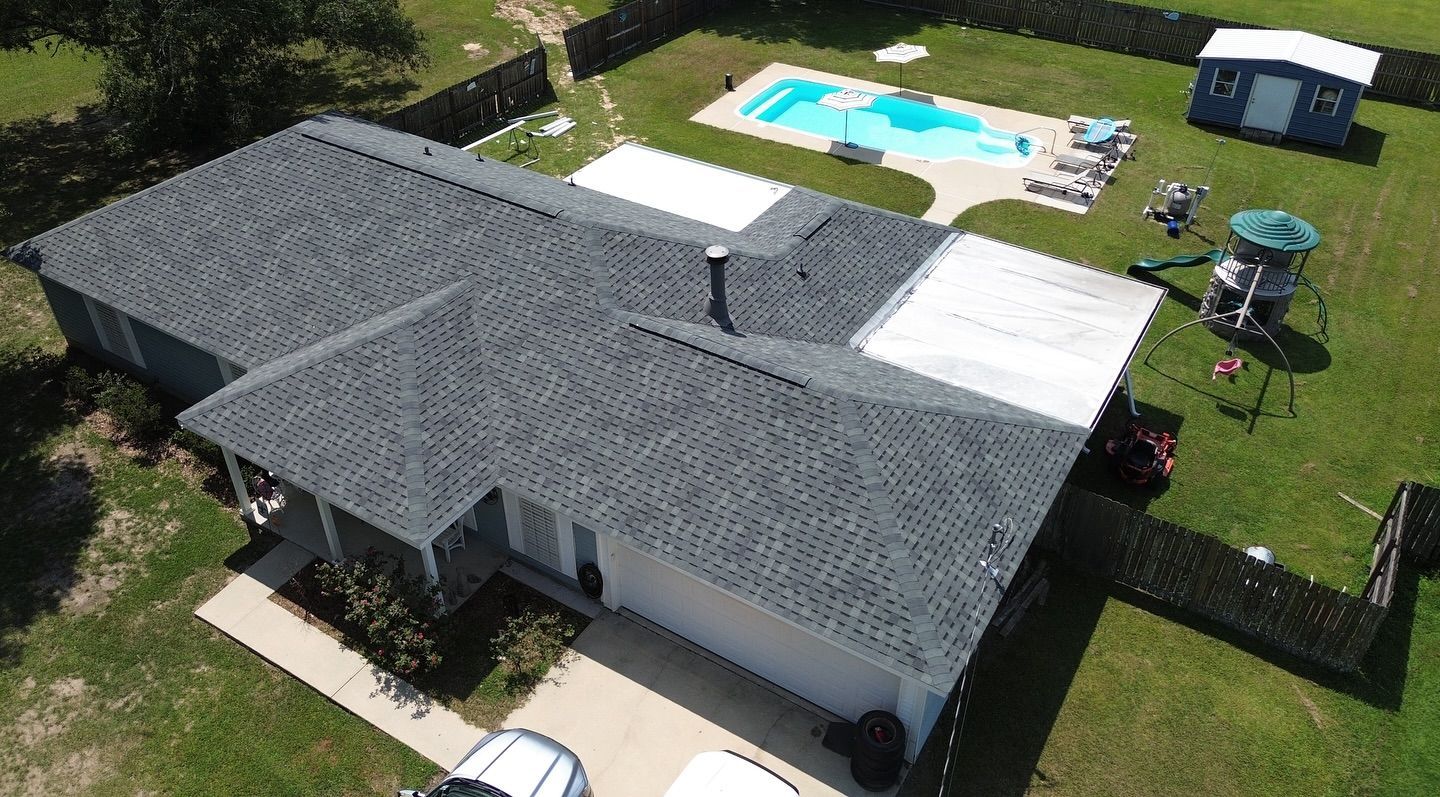 Aerial view of a house with a dark gray roof, a pool, and a yard with green grass.
