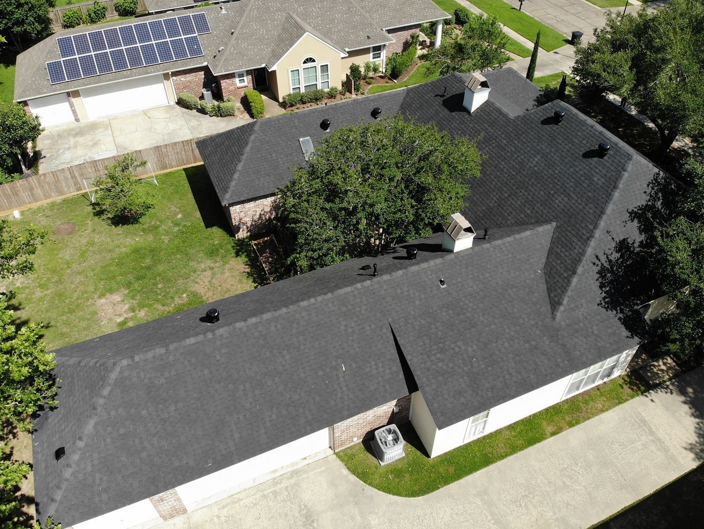 Overhead view of a house with a dark gray roof, surrounded by trees and a grassy lawn.